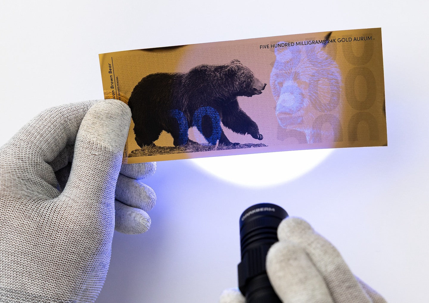 a blacklight held at the center of a half gram gold aurum bill revealing hidden UV designs