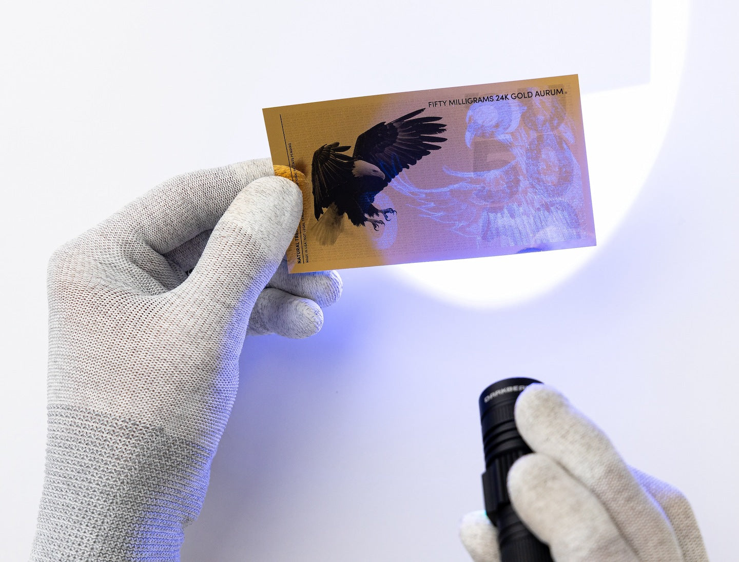 a black light held at the right of a 50mg gold aurum bill revealing the hidden UV design a majestic bald eagle