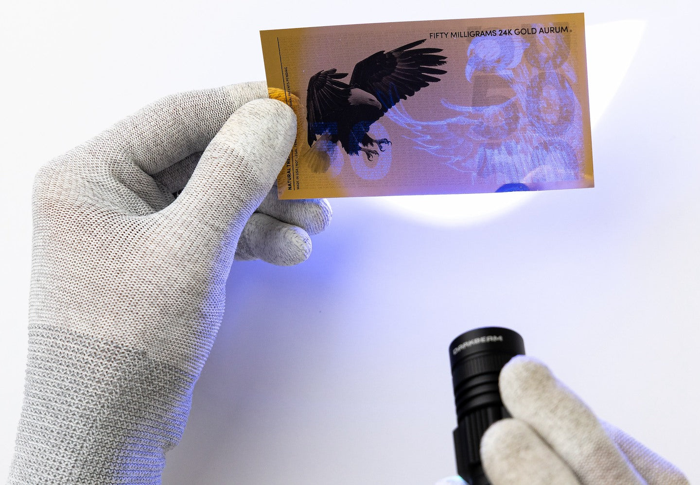 a black light held at the center of a 50mg gold aurum bill revealing the hidden UV features