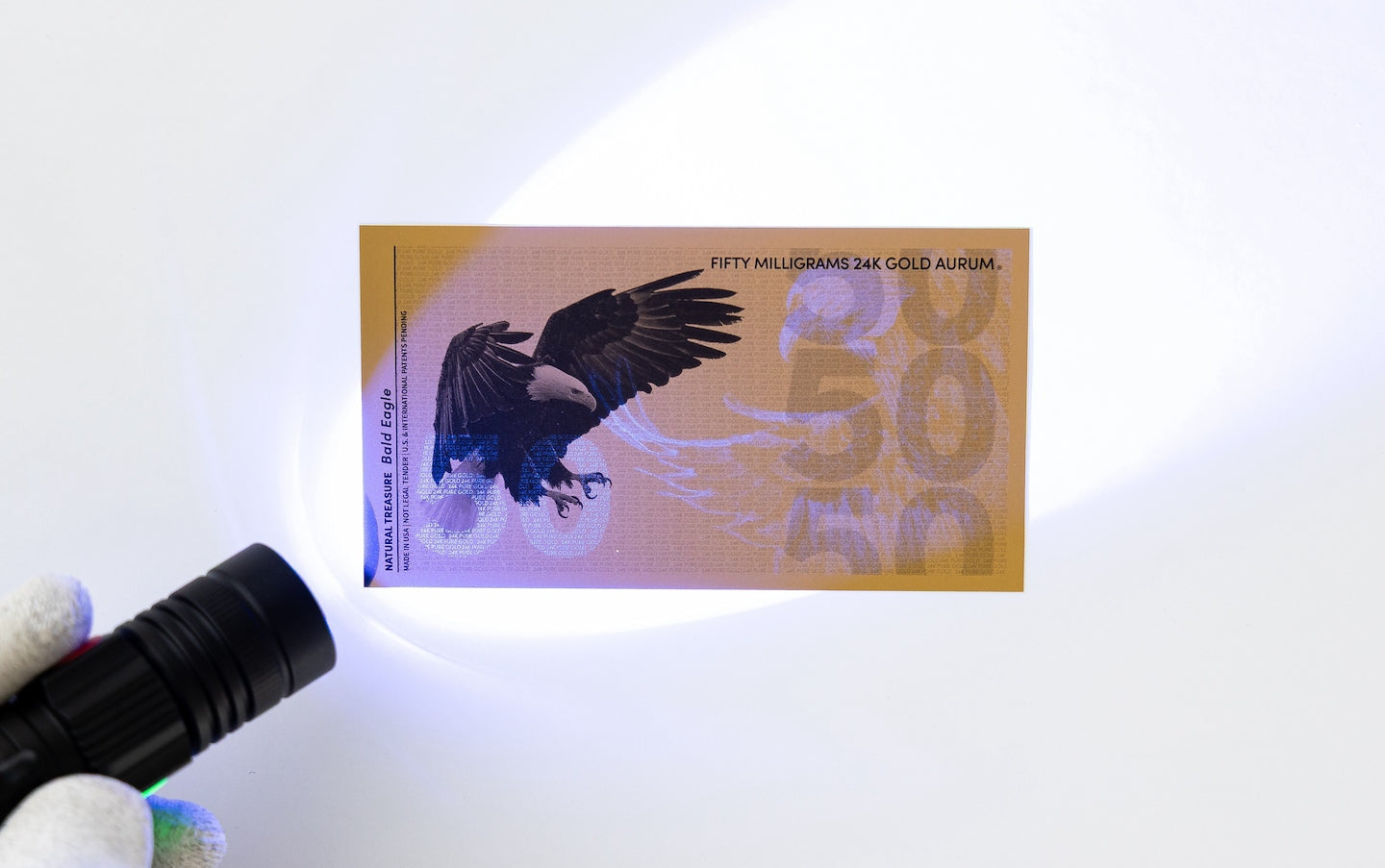 a black light held to the left of a 50mg gold aurum bill revealing the hidden UV features
