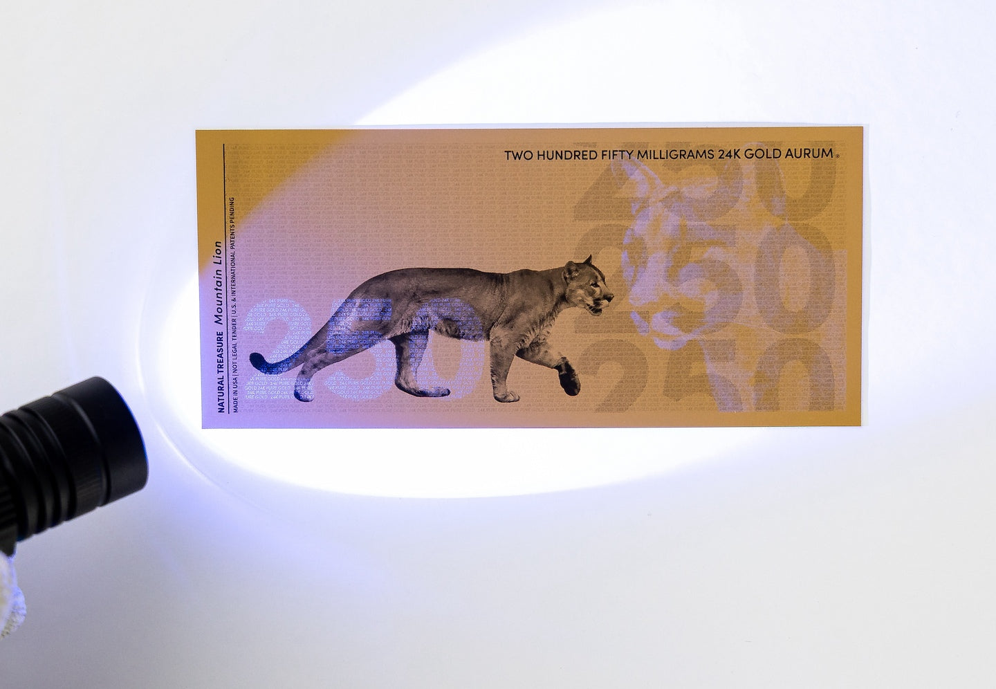 a blacklight held to the left of a 250mg gold aurum bill revealing the hidden UV features