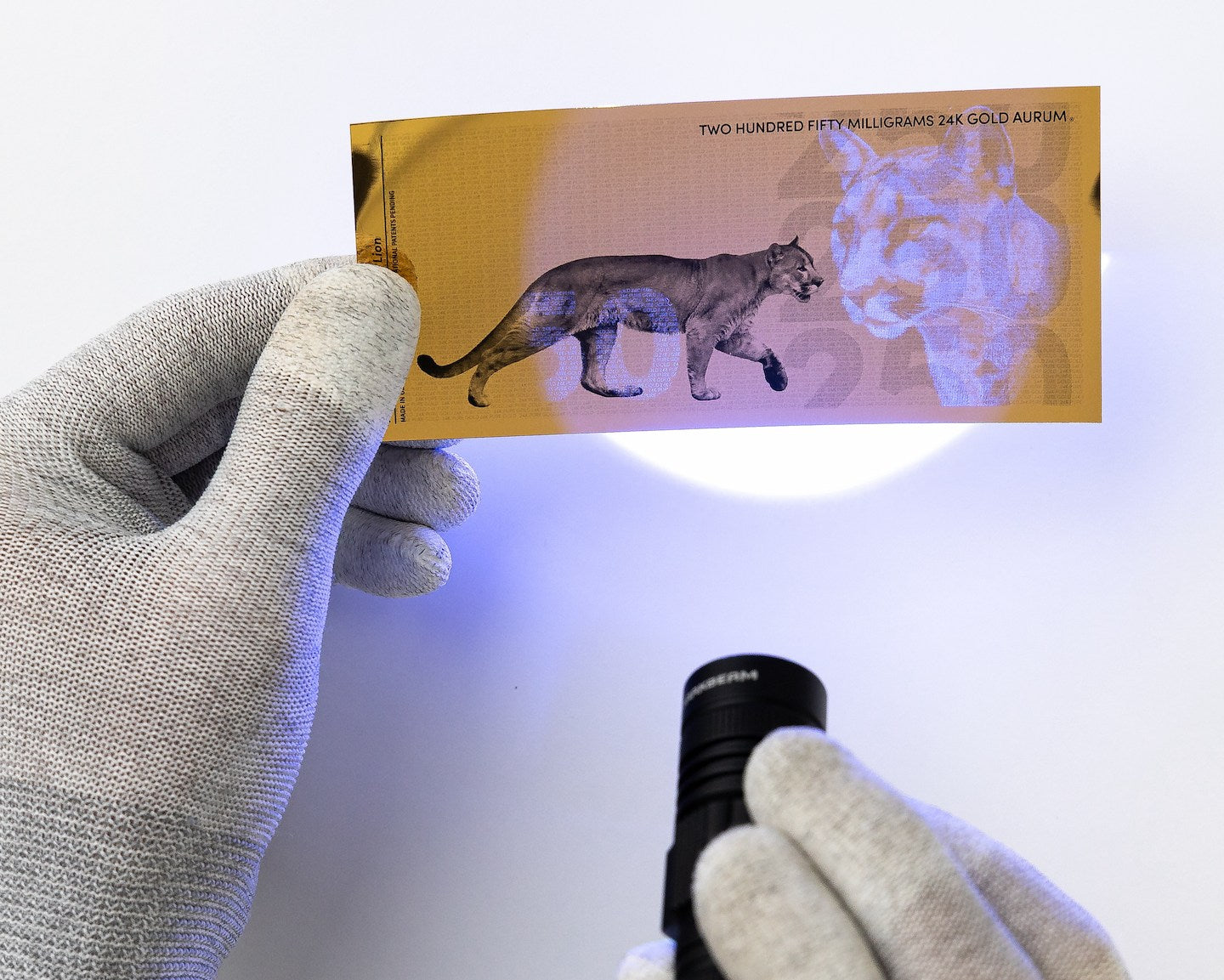 a blacklight held at the center of a 250mg gold aurum bill revealing the hidden UV features
