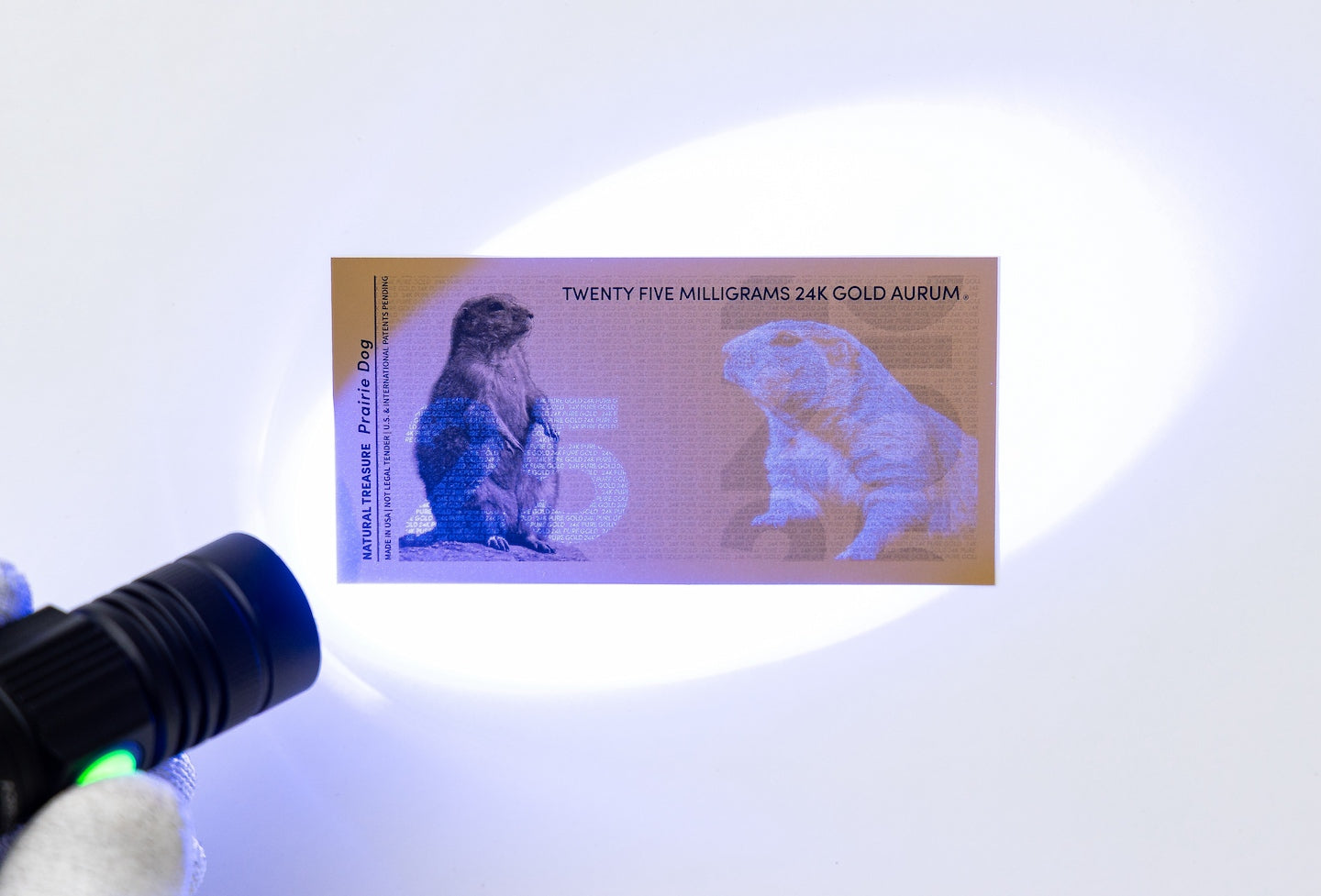 a blacklight held to the left of a gold aurum bill revealing the hidden UV design with a 25 to the left of the bill and a prairie dog on the right side