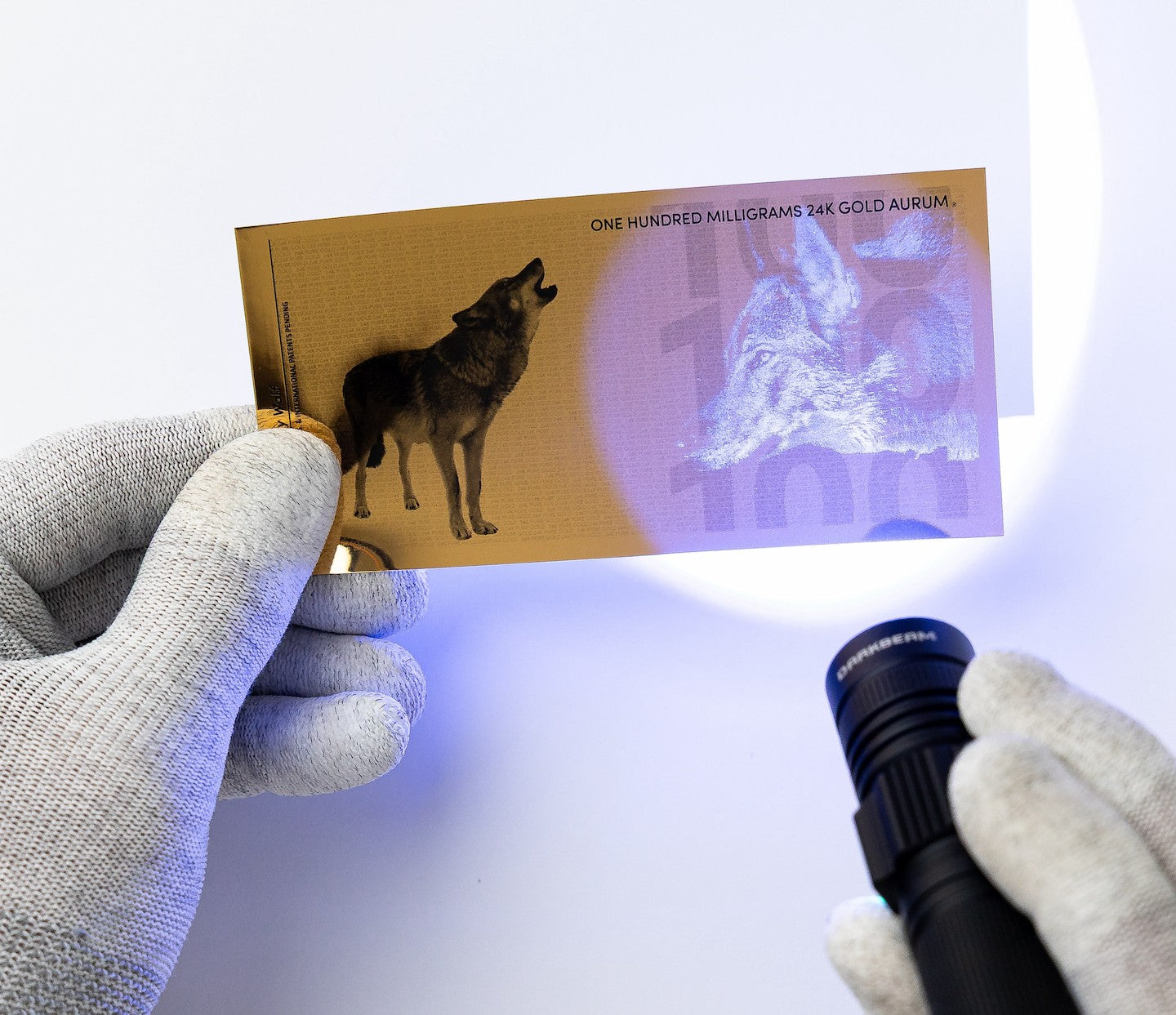 a blacklight held to the right of a 100mg gold aurum bill revealing the hidden UV design highlighting a gray wolf head
