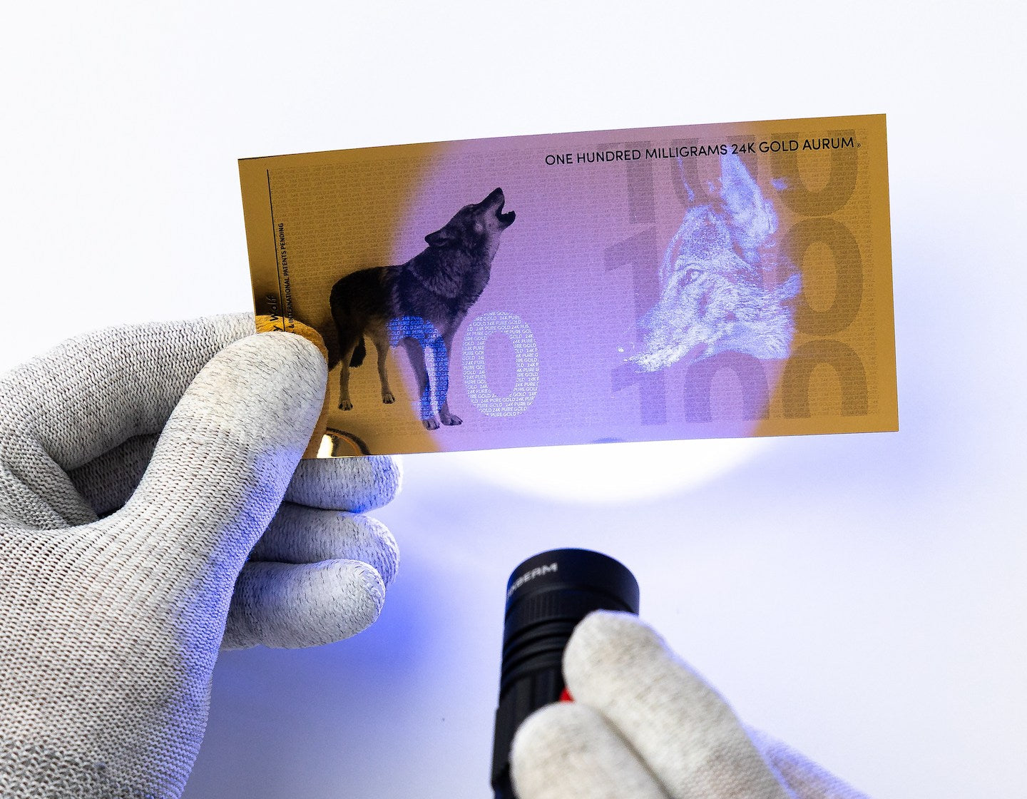 a blacklight held at the center of a 100mg gold aurum bill revealing the hidden UV features