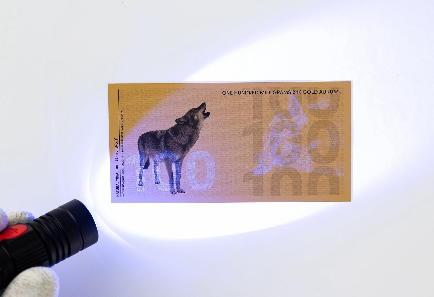 a blacklight held to the left of a 100mg gold aurum bill revealing the hidden UV features